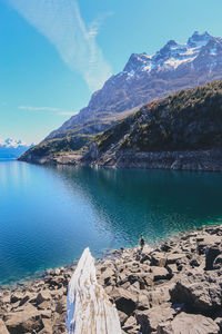 Mid distance view of hiker standing on rock by lake during sunny day