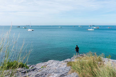 Rear view of man standing on rocky shore against sky