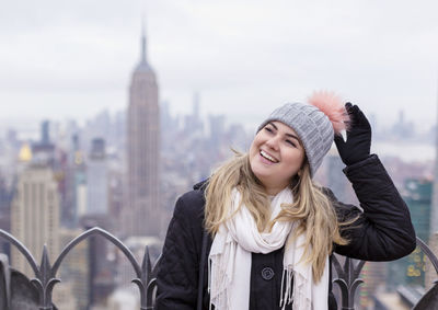 Portrait of smiling young woman against empire state building in city during winter