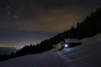 Snow covered cabin against sky at night