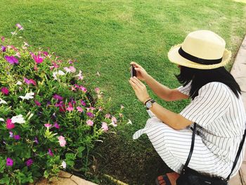 Woman crouching while clicking picture of pink flowers by mobile phone