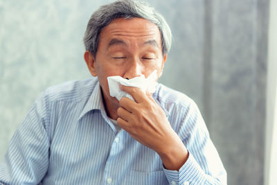 Front view of senior man covering mouth against wall