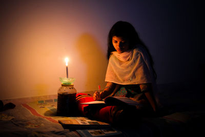 Girl sitting on table against illuminated lamp