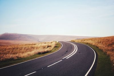 Road passing through field against sky