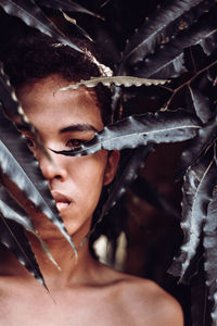  portrait of shirtless teenage girl looking through leaves at park