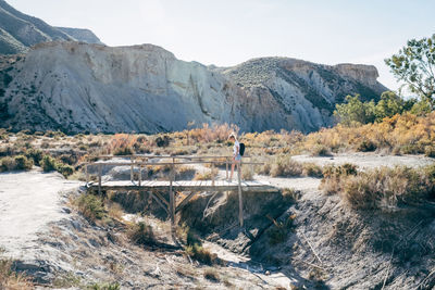 Woman walking on boardwalk by mountain against sky