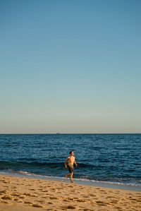 Full length of man running on beach against clear sky