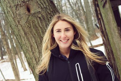 Portrait of smiling young woman wearing warm clothing in forest during winter