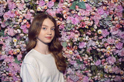 Portrait of a teenage girl with long hair in a white sweater against a wall of flowers