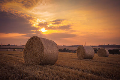 Hay bales on landscape against sky during sunset