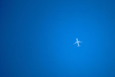 Low angle view of airplane flying against clear blue sky