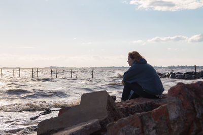 Woman sitting on rock by sea against sky