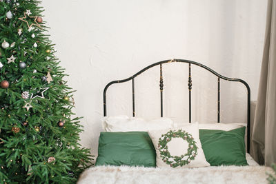 A bed with a beige plaid and green pillows and a christmas tree. new year's winter home interior