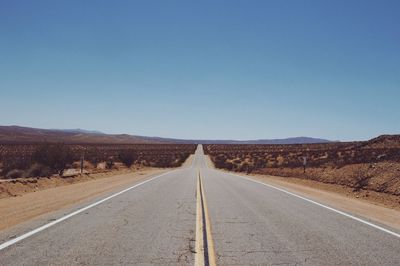 Empty road along landscape against clear sky