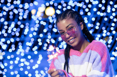 Cheerful black woman with braided hairstyle and pink glasses enjoying christmas lights