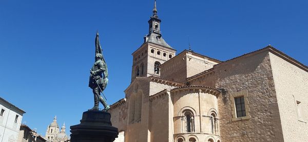 Low angle view of statue amidst buildings against clear blue sky