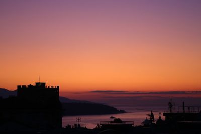 Silhouette buildings by sea against romantic sky at sunset