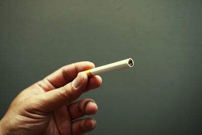 Close-up of hand holding cigarette against wall