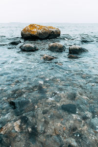 Pebbles on rock in sea against sky