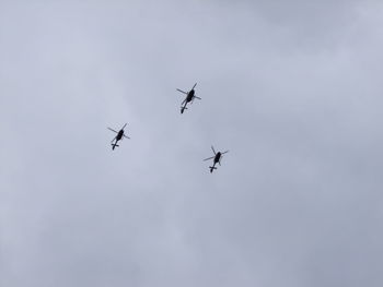 Low angle view of silhouette helicopters flying against cloudy sky