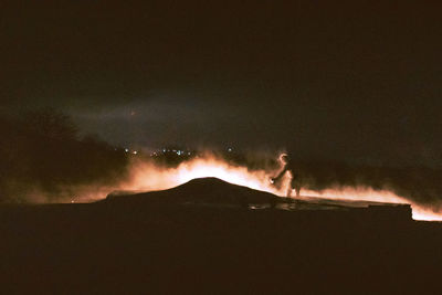 Silhouette people on illuminated land against sky at night