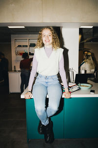 Portrait of smiling young woman sitting on dining table at college dorm