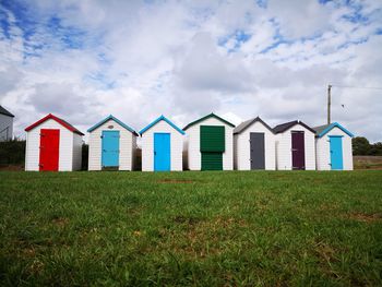 Beach huts on grassy field against cloudy sky