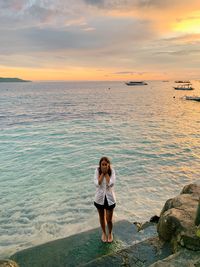 Rear view of woman standing at beach against sky during sunset