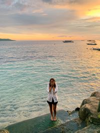 Full length of woman standing at beach against sky during sunset