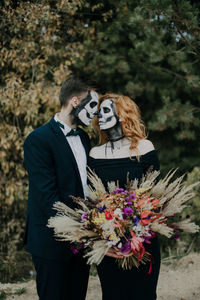 A couple in love celebrates halloween in costumes and makeup with a bouquet of dried flowers