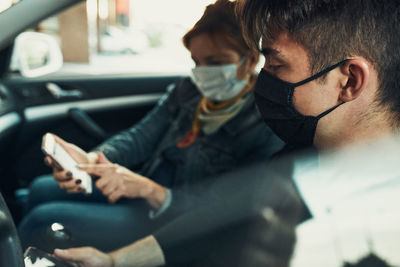 Man and woman sitting in a car using smartphones wearing the face masks to avoid virus infection