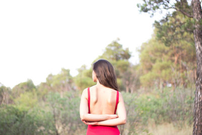 Rear view of woman standing amidst trees against clear sky