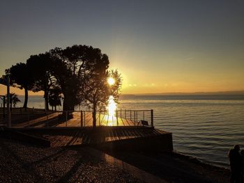 Silhouette trees by sea against sky during sunset