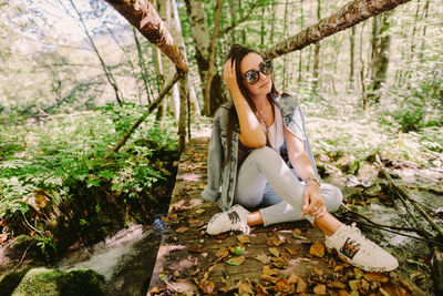 Portrait of smiling young woman sitting on land in forest