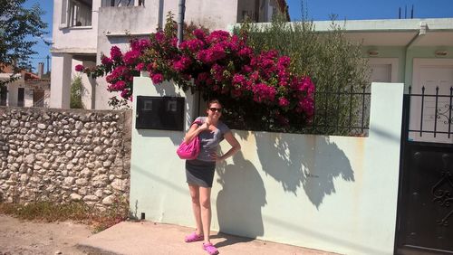 Woman standing by pink flowering plant against building