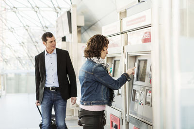 Businessman looking at colleague buying ticket at railroad station