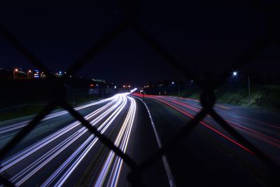 Light trails on road seen through chainlink fence