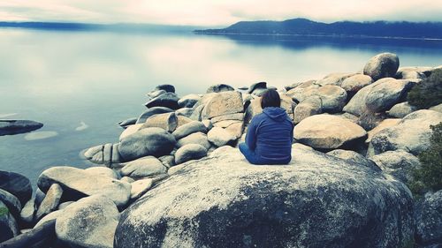 Rear view of person sitting on rock by river