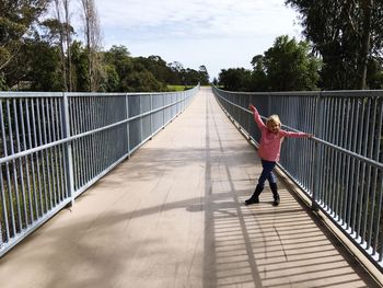 Full length of girl standing on bridge amidst trees against sky