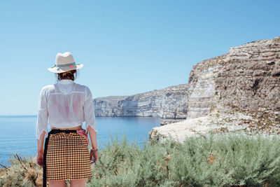 Rear view of woman standing on rock against sky