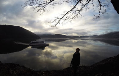 Silhouette man standing by lake against sky