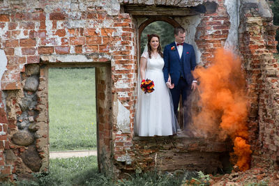 Full length of newlywed couple standing by abandoned built structure