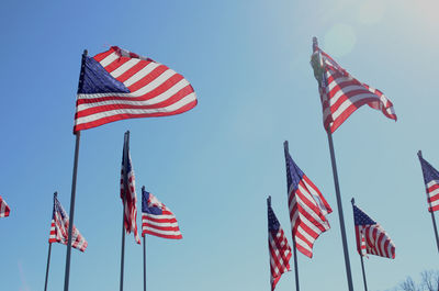 Low angle view of american flags waving against clear blue sky