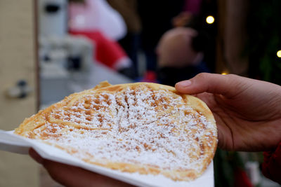 Close-up two hands holding one big tasty waffle with icing sugar. santa at advent christmas market. 