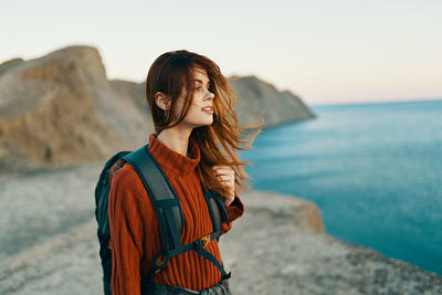 Young woman standing at beach against sky