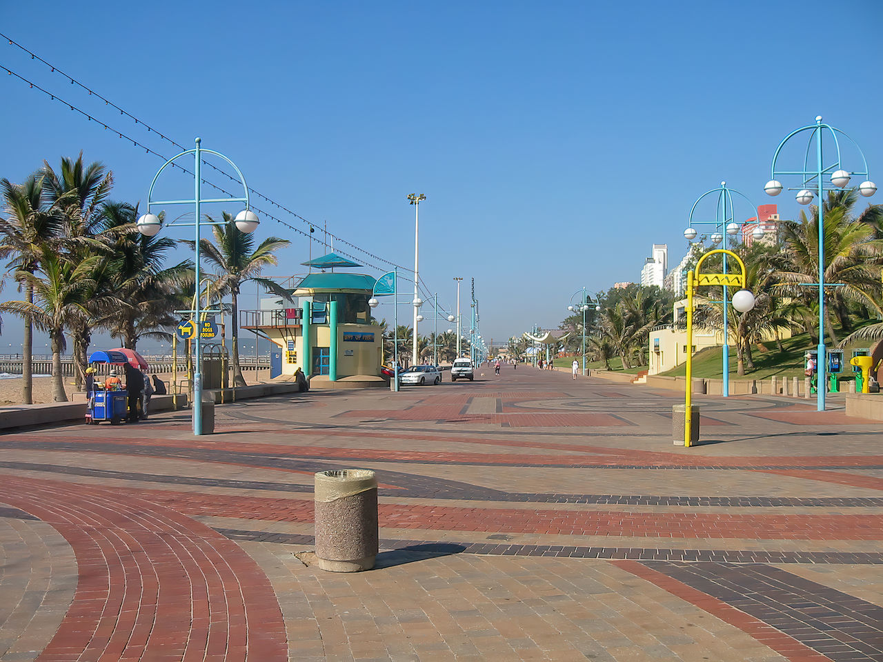 walkway, city, boardwalk, palm tree, sky, town square, tropical climate, architecture, tree, street, clear sky, nature, town, public space, neighbourhood, plaza, downtown, residential area, day, footpath, road, built structure, plant, sunny, building exterior, blue, travel destinations, no people, road surface, outdoors, transportation, sunlight, street light, vacation, travel, urban area