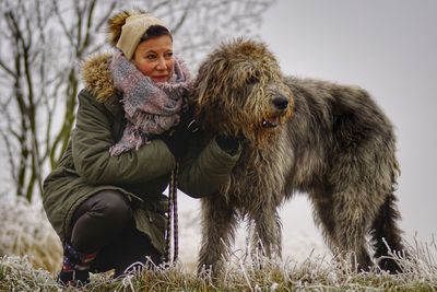 Woman crouching by irish wolfhound on field during winter