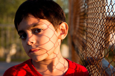 Close-up of portrait of boy with chainlink fence shadow on face 