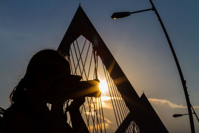 Silhouette woman photographing by bridge at sunset