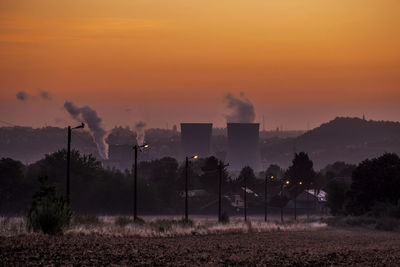 Smoke emitting from factory against orange sky